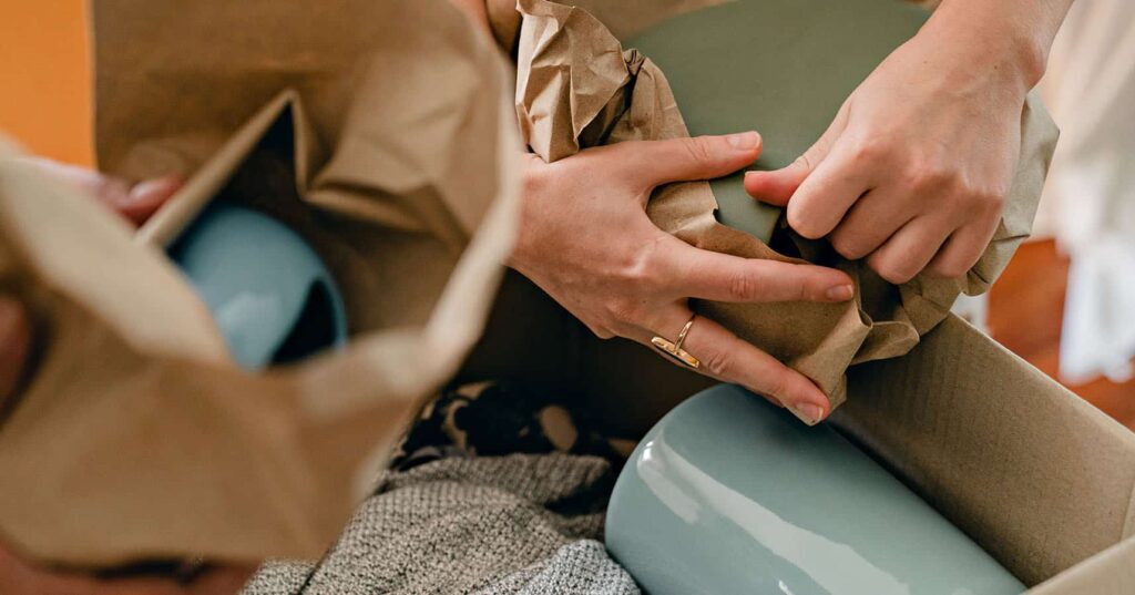 Hands wrapping ceramic items in brown paper
