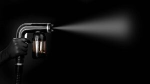 Handheld paint sprayer spraying mist on black background