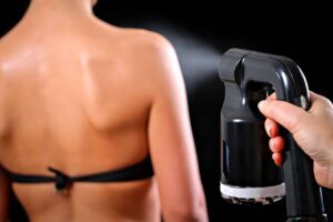 Hand spraying tanning solution on woman's back