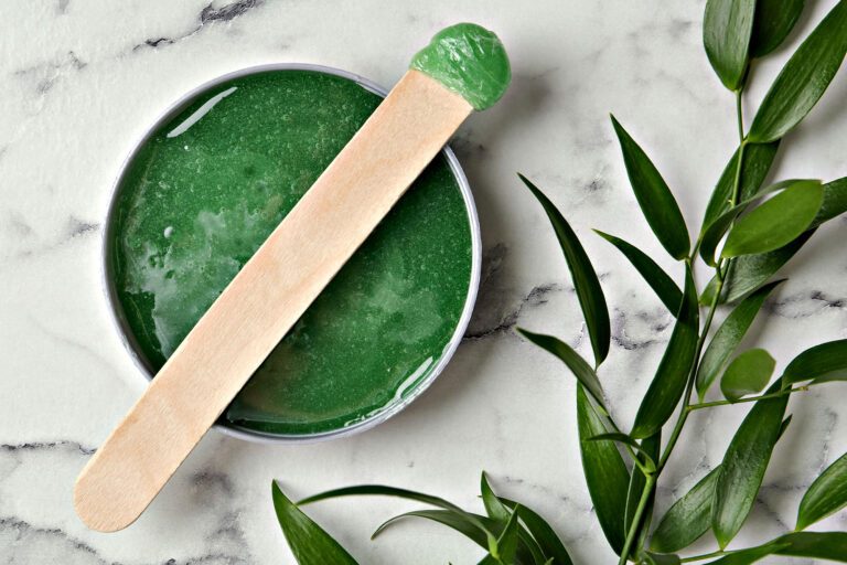 Green waxing paste with wooden spatula on marble background