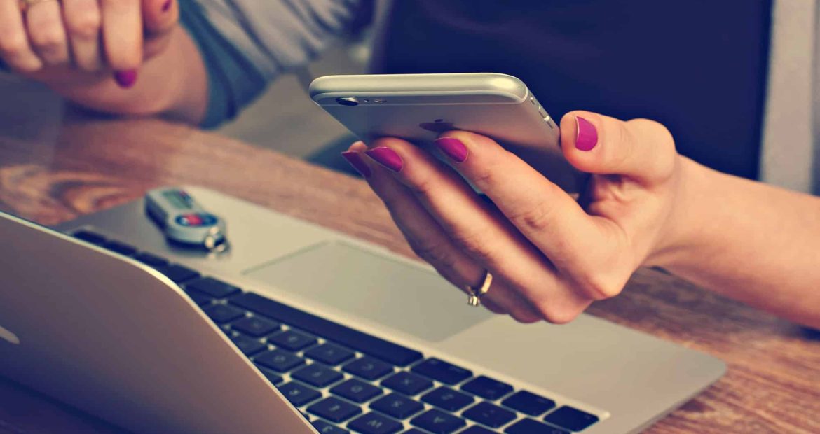 Person using smartphone and laptop with a USB drive nearby