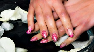 Pink sparkly manicured nails with flower petals in water