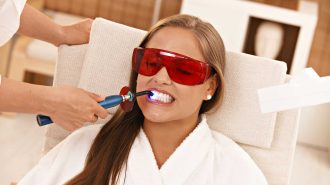 Woman receiving dental laser whitening treatment with red protective glasses